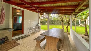 Un patio al aire libre con mesa y sillas de madera, un muro de ladrillo y vistas a un jardín.