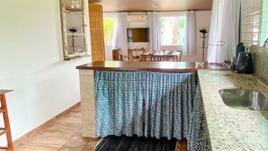 A kitchen with a wooden ceiling, a tiled floor, a patterned tablecloth-covered dining table, and a coffee maker on the counter. - Casa Recanto da Armação (Florianopolis)