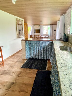 Una cocina con techo de madera, suelo de baldosas, una mesa de comedor cubierta con mantel estampado y una cafetera en la encimera.