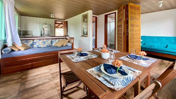 Una habitación acogedora con techo de madera, una mesa de comedor dispuesta con platos, servilletas y cubiertos, y un sofá azul con cojines estampados.