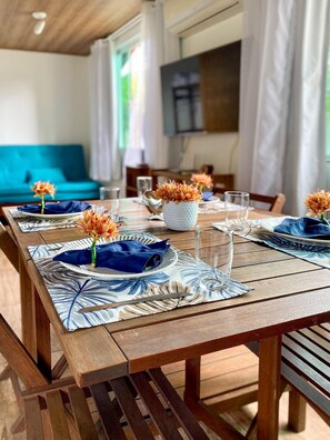 Une table de salle à manger en bois, mise avec des serviettes, des assiettes et des verres bleus, et décorée de fleurs oranges dans des vases.