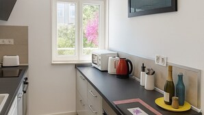 Cozinha moderna com janela, micro-ondas, chaleira e um pequeno espaço de refeições com uma cadeira.