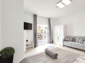 Een moderne, goed verlichte woonkamer met een grijze bank, een aan de muur bevestigde televisie en een groot raam met gordijnen.