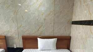 A neatly made bed with a wooden headboard and a white pillow, set against marble-patterned walls. - Thulee Luxury Hotel - Phu My (Ho Chi Minh City)