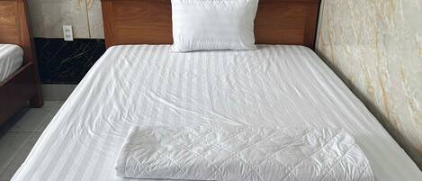 A neatly made bed with a wooden headboard and a white pillow, set against marble-patterned walls.