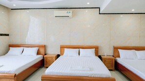 A hotel room with three wooden beds, each with a wooden headboard and white bedding. There is a ceiling-mounted air conditioning unit and a small wooden nightstand with drawers next to each bed. - Thulee Luxury Hotel - Phu My (Ho Chi Minh City)