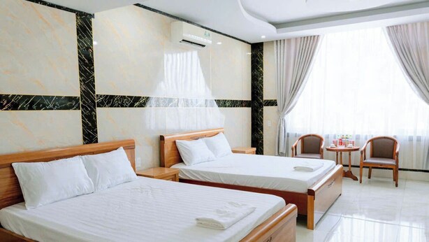 A hotel room with two beds, a small table, a chair, and a window with curtains. - Thulee Luxury Hotel - Phu My (Ho Chi Minh City)