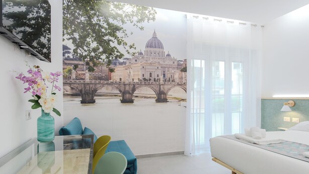 A hotel room with a bed, a desk with a vase of flowers, a chair, and a mural of a bridge and building. - Domus Suites (Rome)