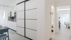 A modern kitchen with white cabinets and black handles, a dining area with a table and chairs, and a bedroom with a bed and a nightstand. - Domus Suites (Rome)