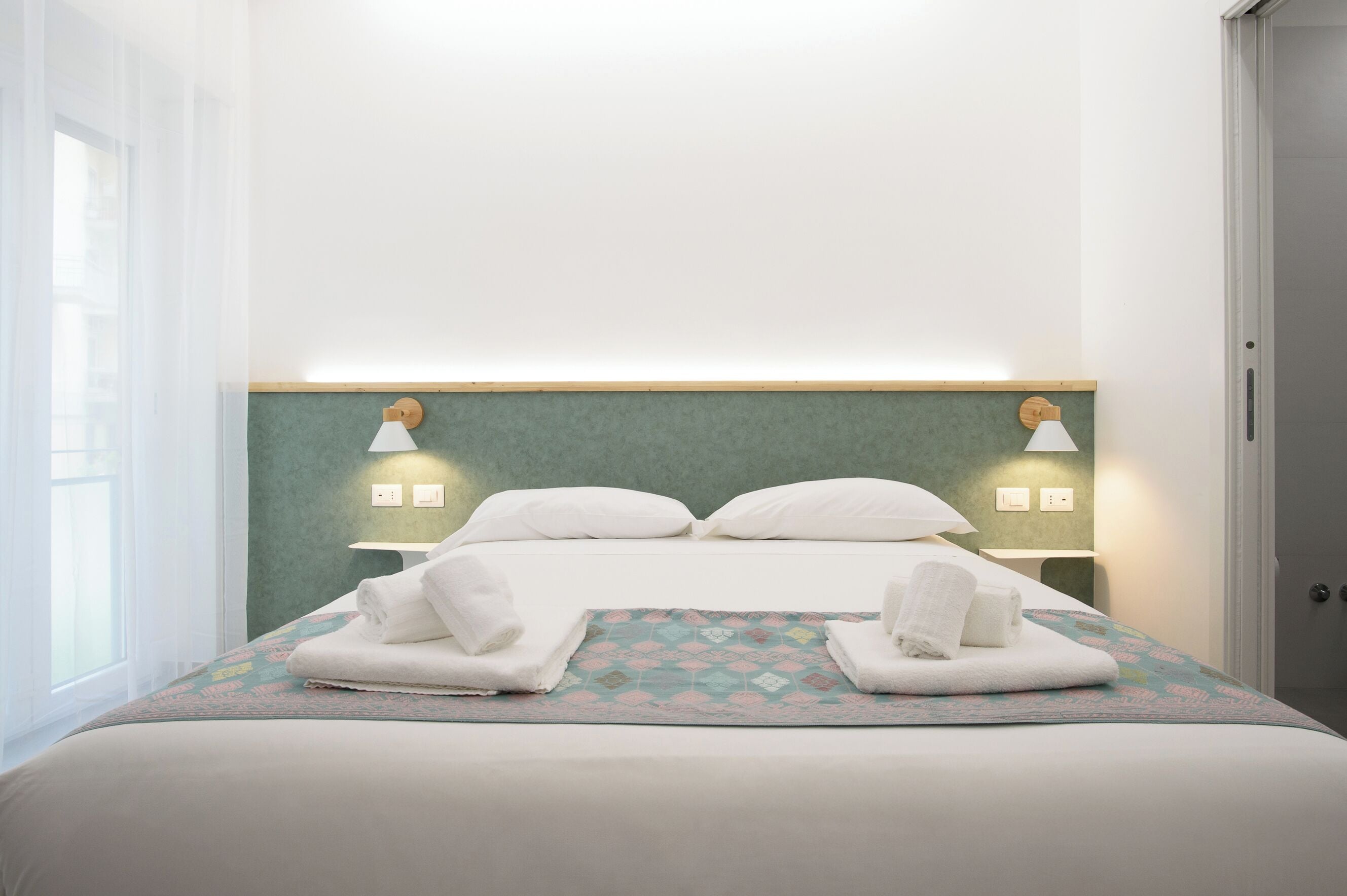 A neatly made bed with white linens and two towels folded on the bed.