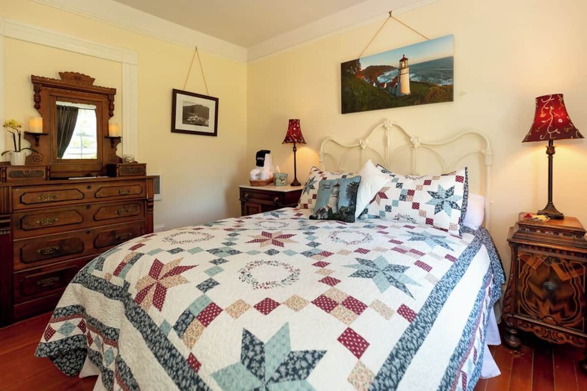 A bedroom with a large bed, a dresser, a nightstand, a lamp, and a painting on the wall.