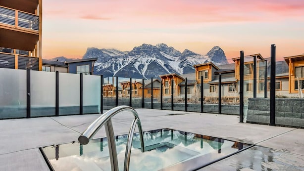 Una piscina en la azotea con fondo de cristal, rodeada de edificios modernos y montañas al fondo.