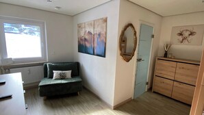 A room with a green sofa, a painting, a mirror, a wooden cabinet, and a window with a view of a snowy landscape. - "Bergnest", Oberstaufen/Steibis (Oberstaufen)
