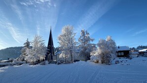 A snow-covered church with a tall steeple and a clock tower, surrounded by snow-laden trees and buildings. - "Bergnest", Oberstaufen/Steibis (Oberstaufen)