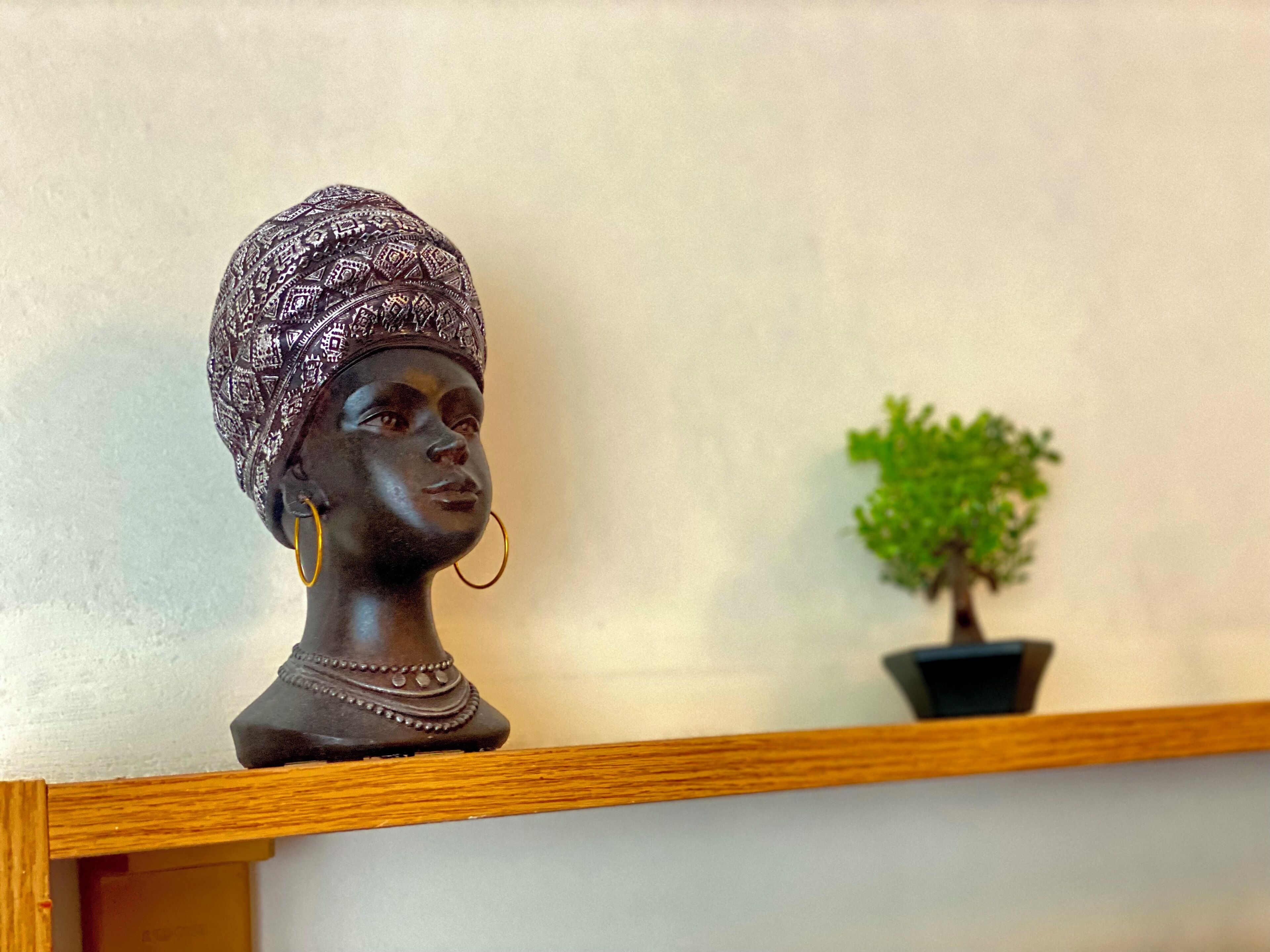 A bust sculpture with intricate patterns on its headpiece, placed on a wooden shelf.