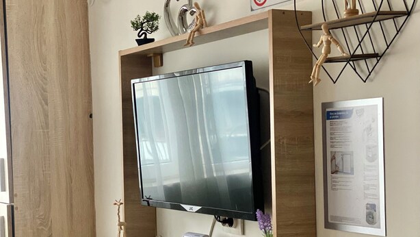 Ett modernt rum med ett TV-bord i trä, en väggmonterad TV, en liten hylla med dekorativa föremål, en skylt med texten ”Rökning förbjuden” och en inramad informationsaffisch.