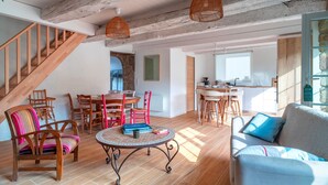 Un vaste espace de vie comprenant un escalier en bois, une table ronde avec des chaises, un canapé et un coin cuisine.