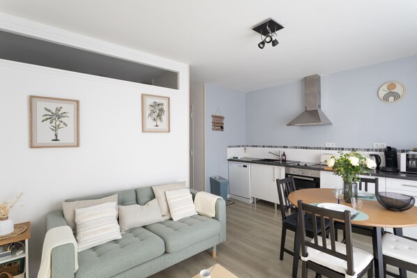 Una sala de estar moderna con un sofá gris, una mesa de comedor con sillas y una zona de cocina con estufa y lavaplatos.