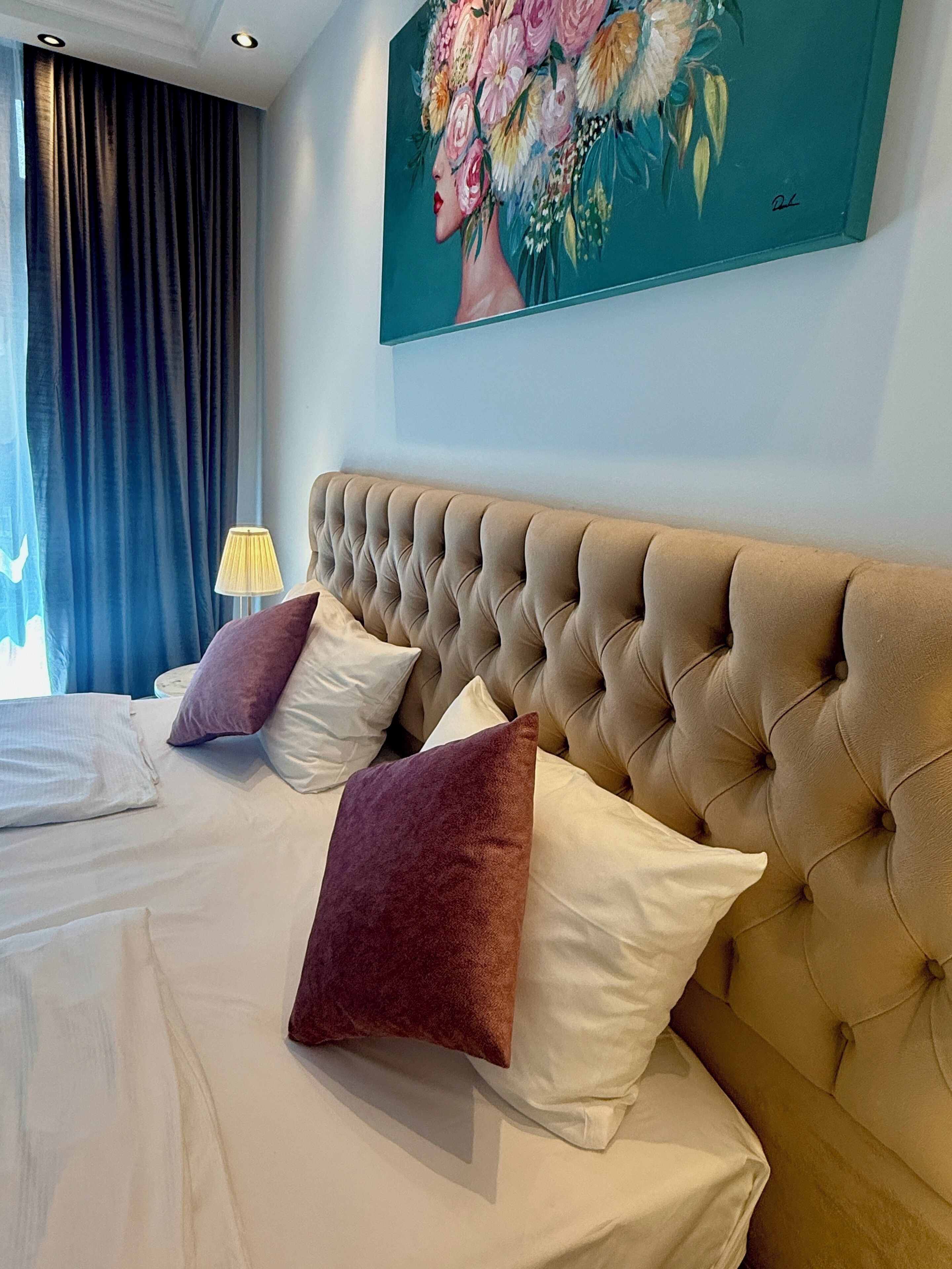 Ein Hotelzimmer mit einer gesteppten Kopfteil, einem großen Blumenbild und einem Bett mit weißen und violetten Kissen.