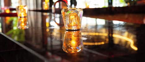 Un área de bar con superficie reflectante, un candelabro de vidrio y una silla roja.
