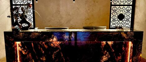 A marble bar with a geometric pattern backdrop, a vase with dried flowers, and a hanging light fixture.