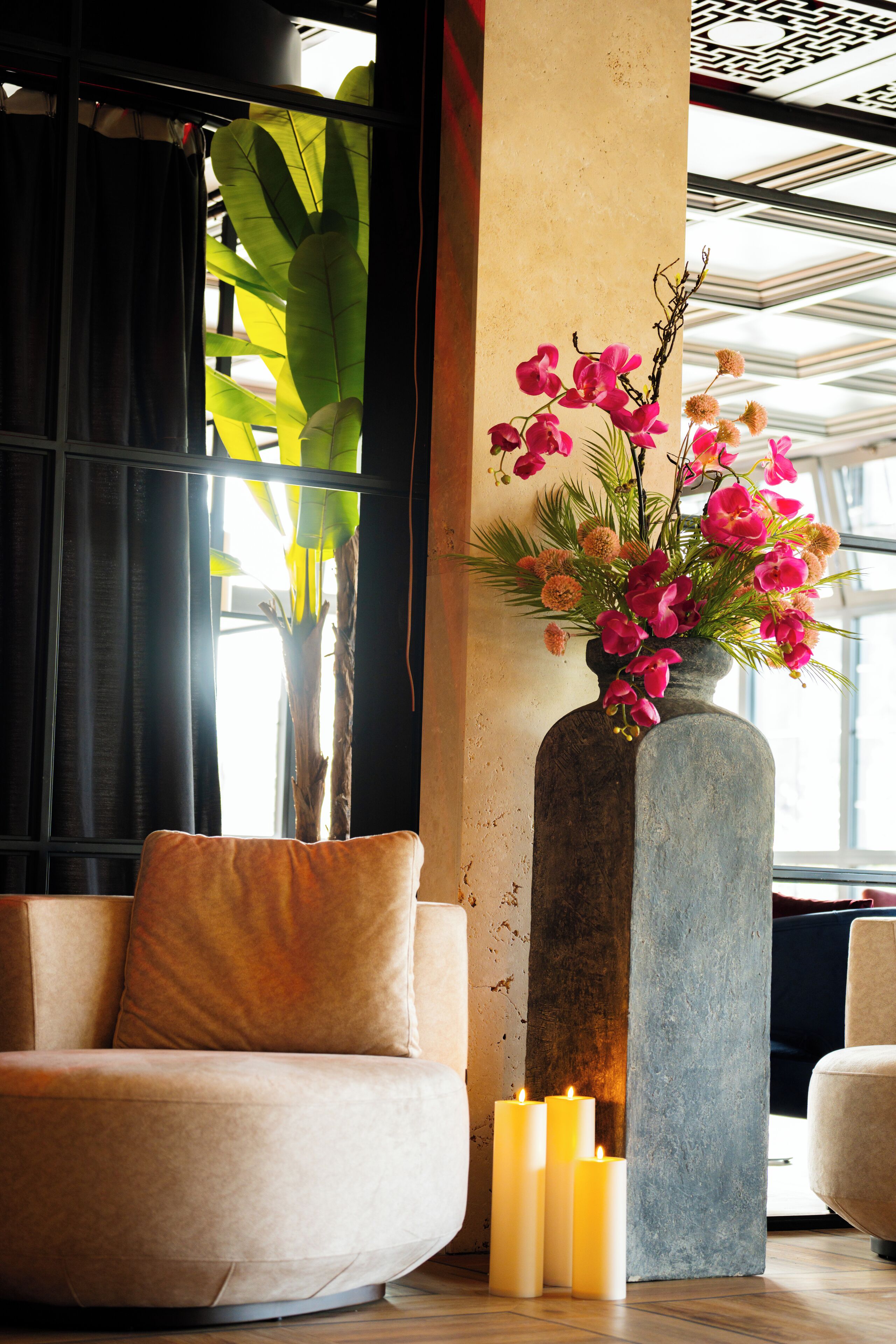 Un intérieur moderne avec un canapé beige, un grand vase rempli de fleurs roses et des bougies posées sur un plancher en bois.