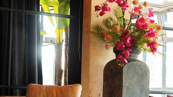 Un intérieur moderne avec un canapé beige, un grand vase rempli de fleurs roses et des bougies posées sur un plancher en bois.