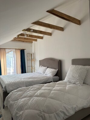 A bedroom with two beds, wooden beams on the ceiling, a window with curtains, and a metal coat rack. - Sweet Vibe Home (Almaty)