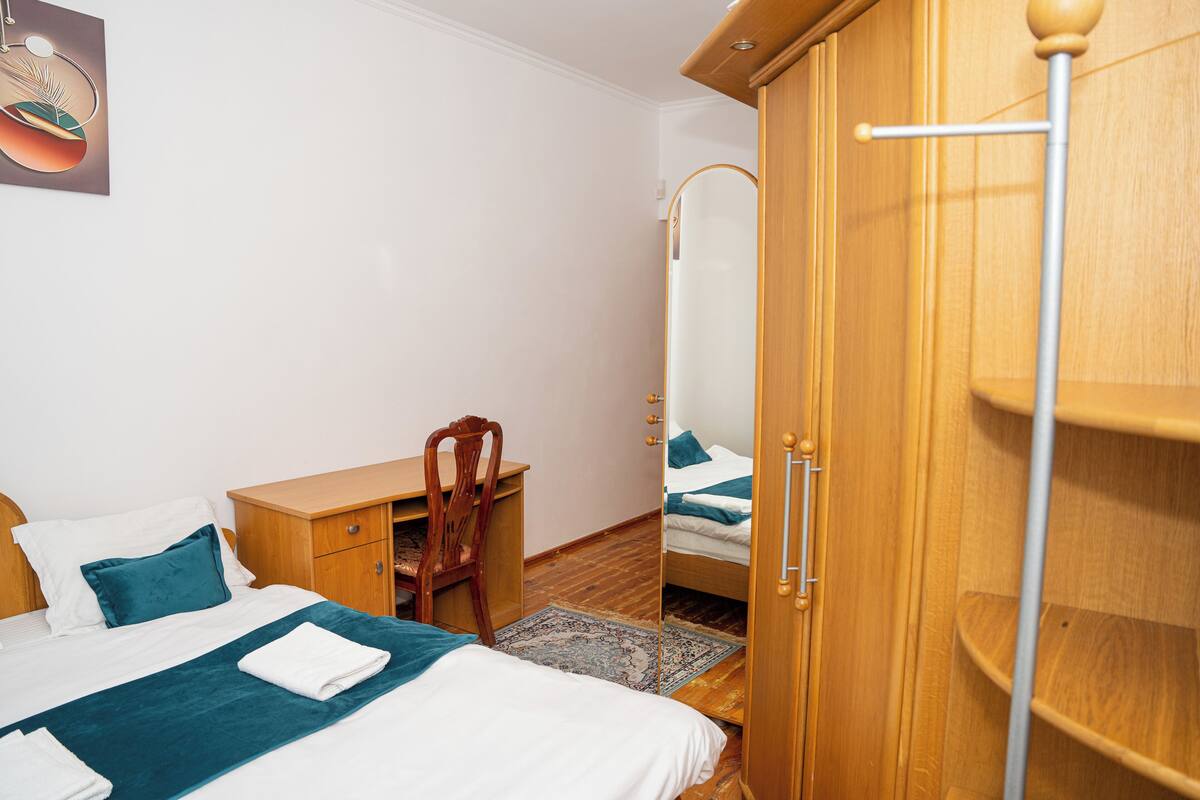 A bedroom with a bed, a desk, a chair, a wardrobe, and a mirror.