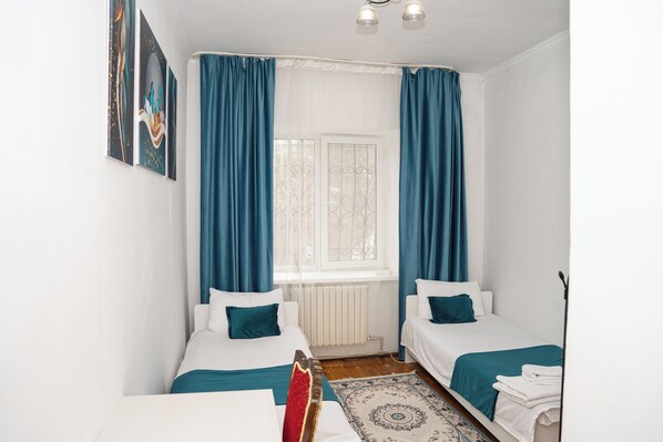 A room with two beds, a window with curtains, a radiator, and a patterned rug.