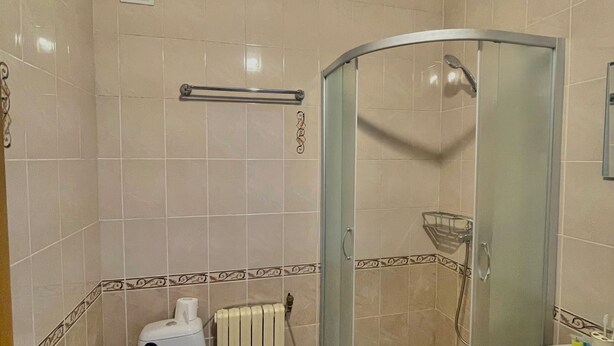 A bathroom with a toilet, a shower with a glass door, a radiator, and a sink. - Sweet Vibe Home (Almaty)