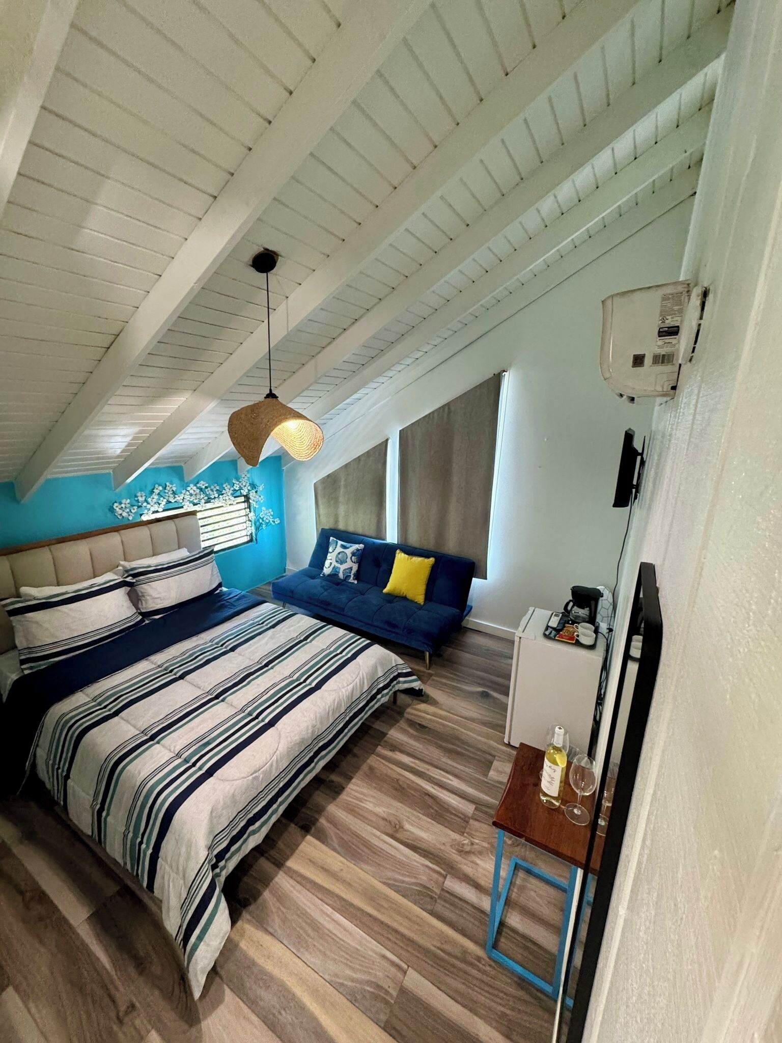 A bedroom with a large bed, a sofa, a small table with a bottle, and a ceiling fan.