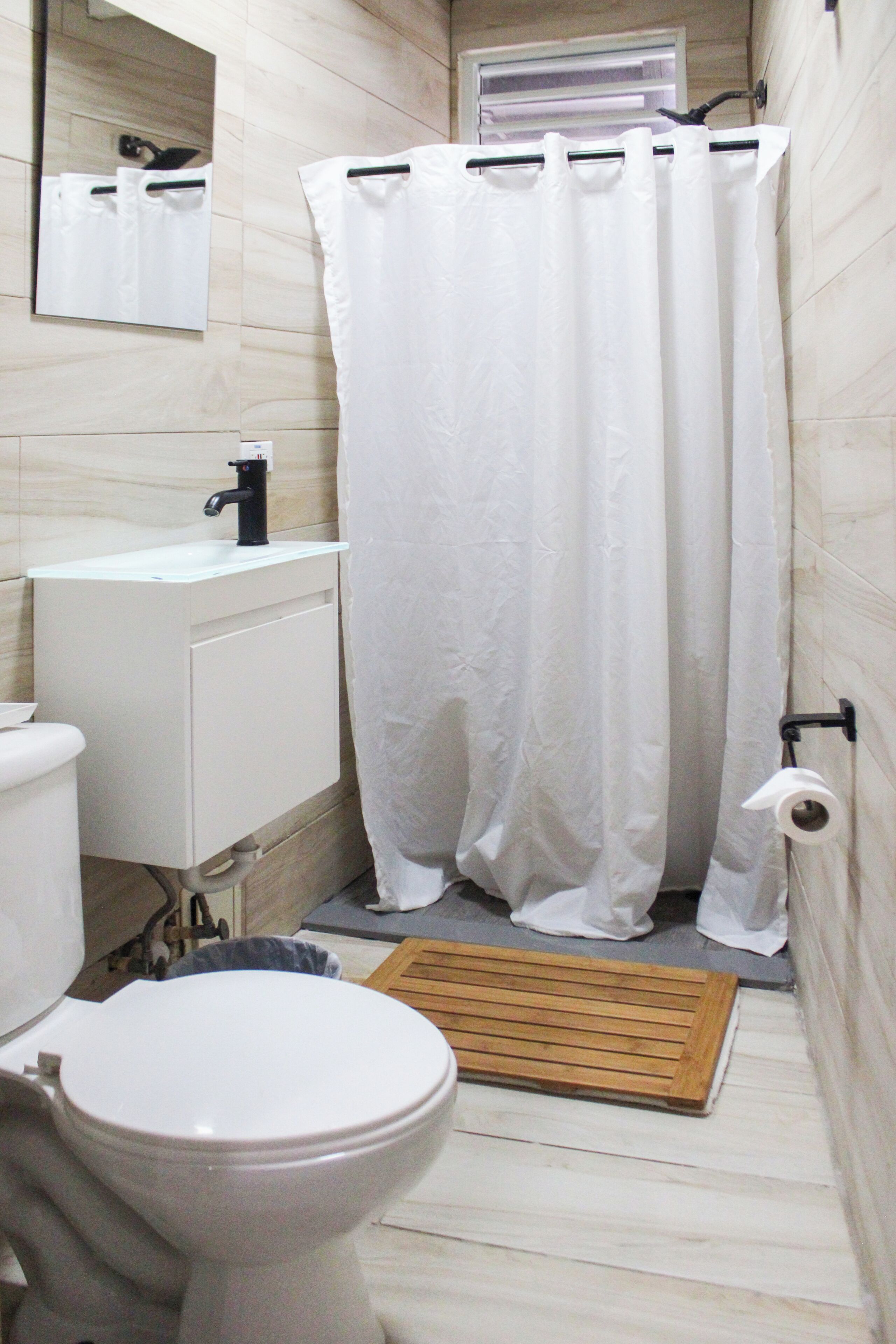 Ein Badezimmer mit Toilette, Waschbecken, Spiegel, Duschvorhang und einer Holzmatte.