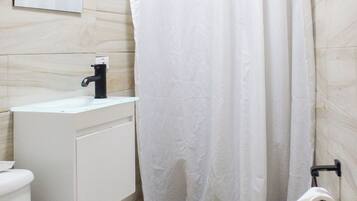 Ein Badezimmer mit Toilette, Waschbecken, Spiegel, Duschvorhang und einer Holzmatte.