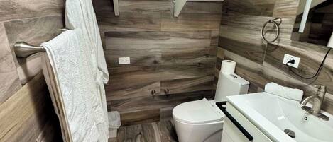 Un baño moderno con piso de madera, tocador blanco y un inodoro.