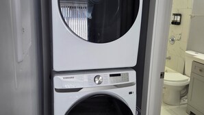 A Samsung front-loading washer and dryer stacked in a narrow space, with a bathroom visible in the background.