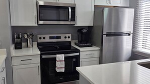 A modern kitchen with white cabinets, a stainless steel microwave, a black stove, and a refrigerator.