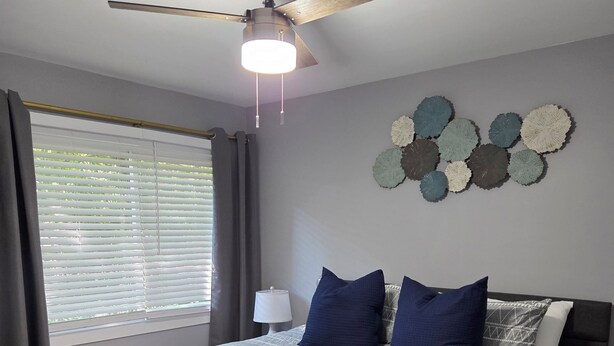 A bedroom with a bed, a ceiling fan, a window with blinds, and a wall decoration.