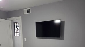 A bedroom with a bed, a TV mounted on the wall, and a door leading to another room.