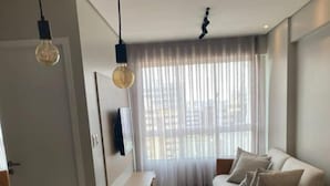 A modern living room with a sofa, coffee table, and chairs. There is a TV mounted on the wall and a window with sheer curtains. - Edificio Promenade II Apt 1108 (Maceio)