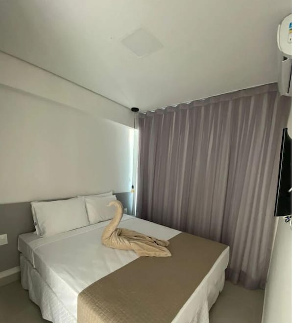 A hotel room with a bed, a swan decoration, and a large window with curtains.