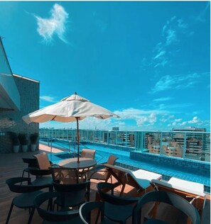 A rooftop pool area with lounge chairs and umbrellas, overlooking a cityscape.