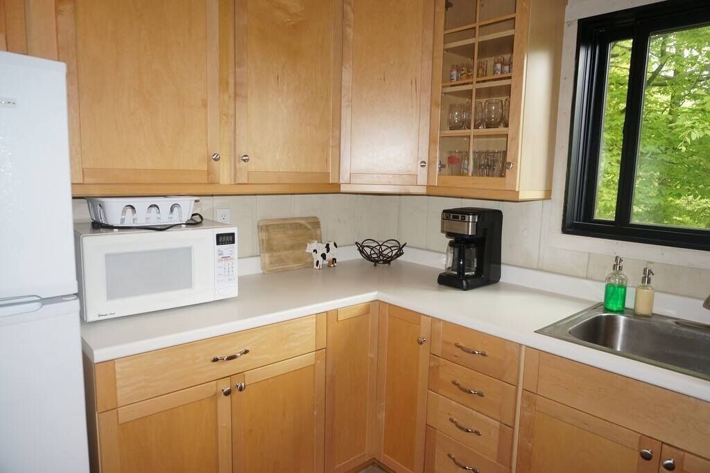 A kitchen with wooden cabinets, a microwave, a coffee maker, and a window with a view of greenery.
