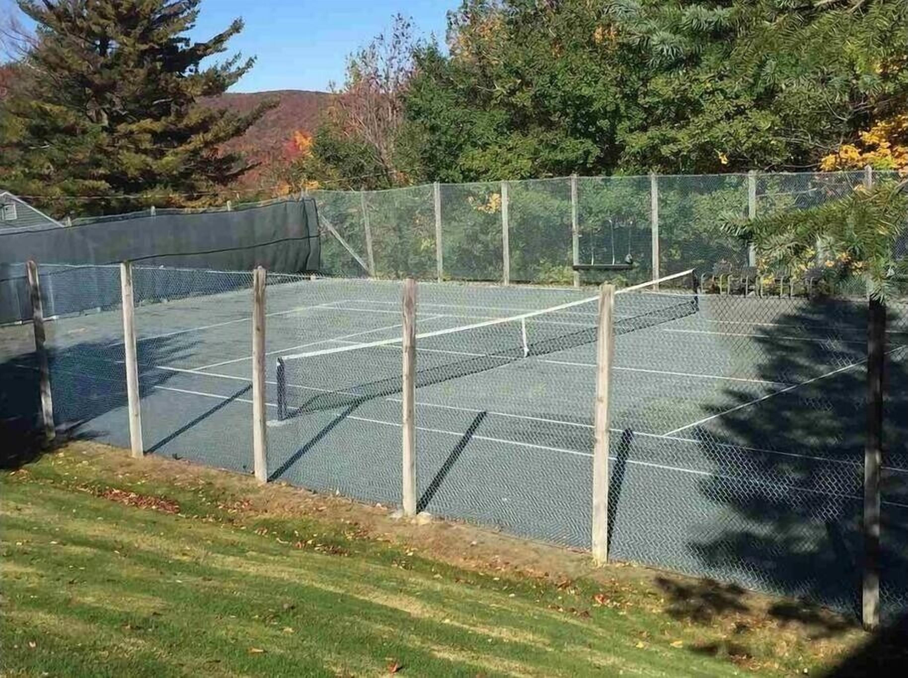 A tennis court enclosed by a chain-link fence with a grassy area in the foreground.