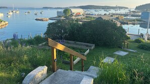 Vista costera con barcos, una escalera de madera y un jardín.