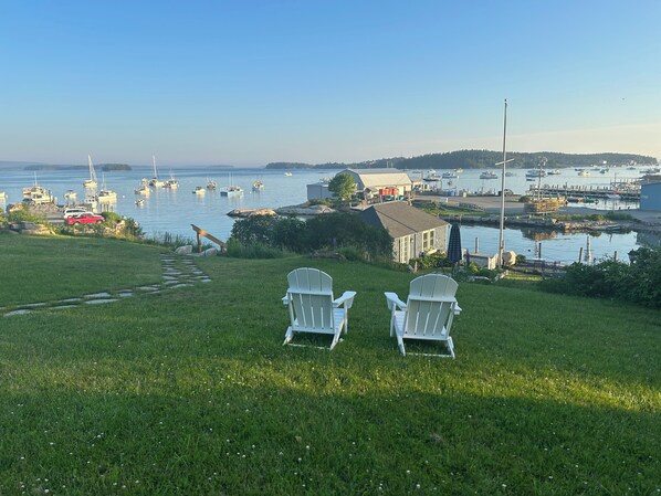 Een gazon met twee witte Adirondack-stoelen gericht op een jachthaven met boten.
