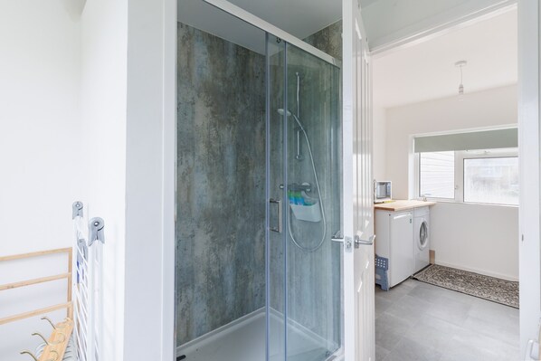 Une salle de bain moderne avec une douche à parois de verre, un lave-linge encastré et un petit coin cuisine.