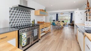 A modern kitchen with a built-in stove, oven, and microwave. There is a dining area with a table and chairs, and a view of the outdoors through a large window. - Sea Breeze Your Coastal Sanctuary in Sandown (Sandown)