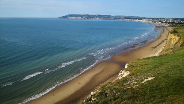 A coastal landscape with a sandy beach, grassy cliffs, and a distant town. - Sea Breeze Your Coastal Sanctuary in Sandown (Sandown)