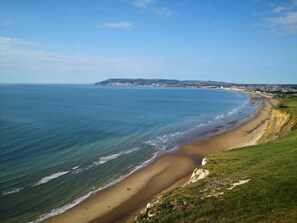 Un paysage côtier avec une plage de sable, des falaises herbeuses et une ville située au loin.